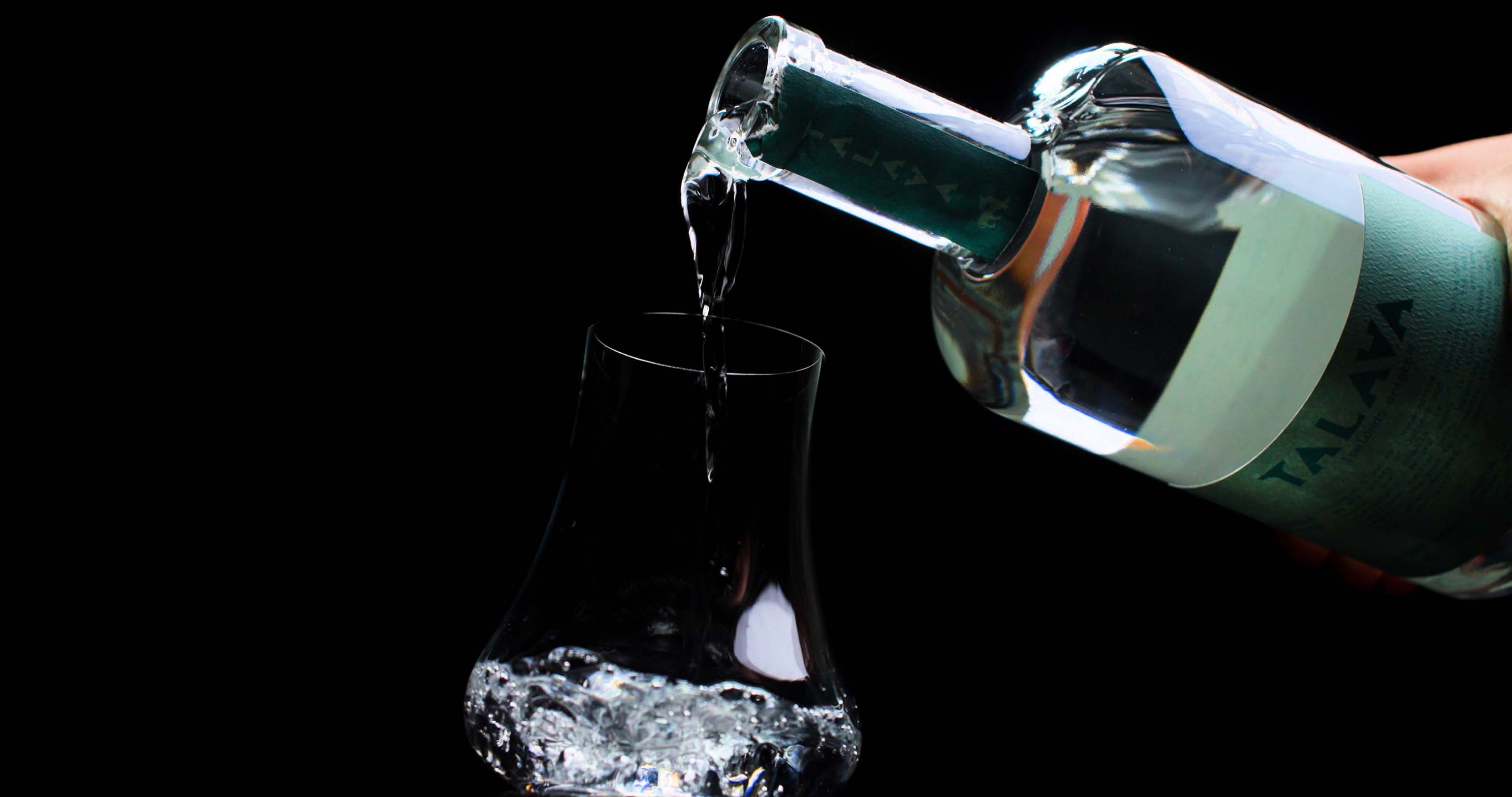 Una botella de tequila Talava posada en un entorno natural, con agaves y montañas al fondo